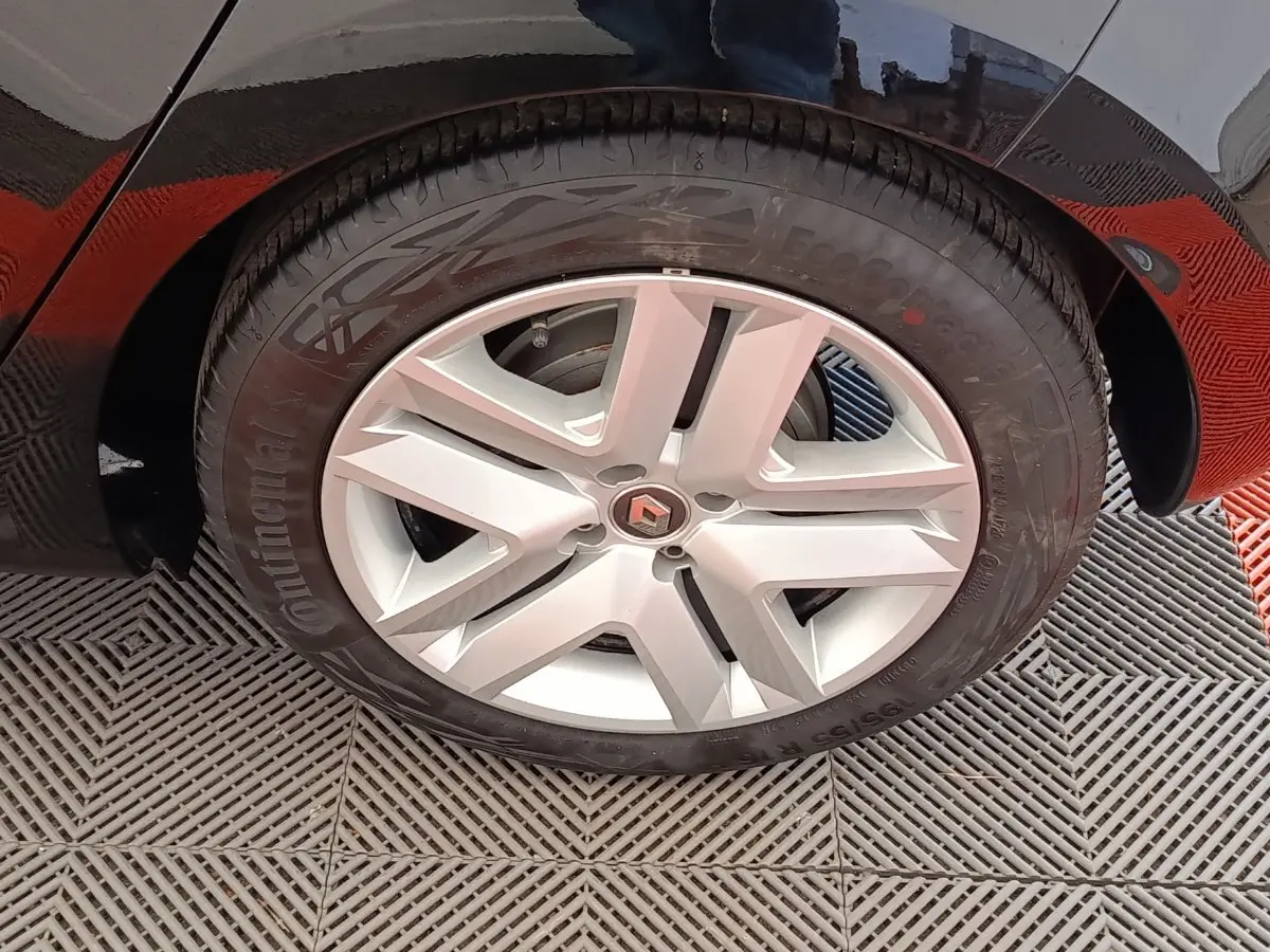 Gros plan sur la roue avant droite d'une Renault Clio blanche, avec jante alliage et logo Renault central visible.