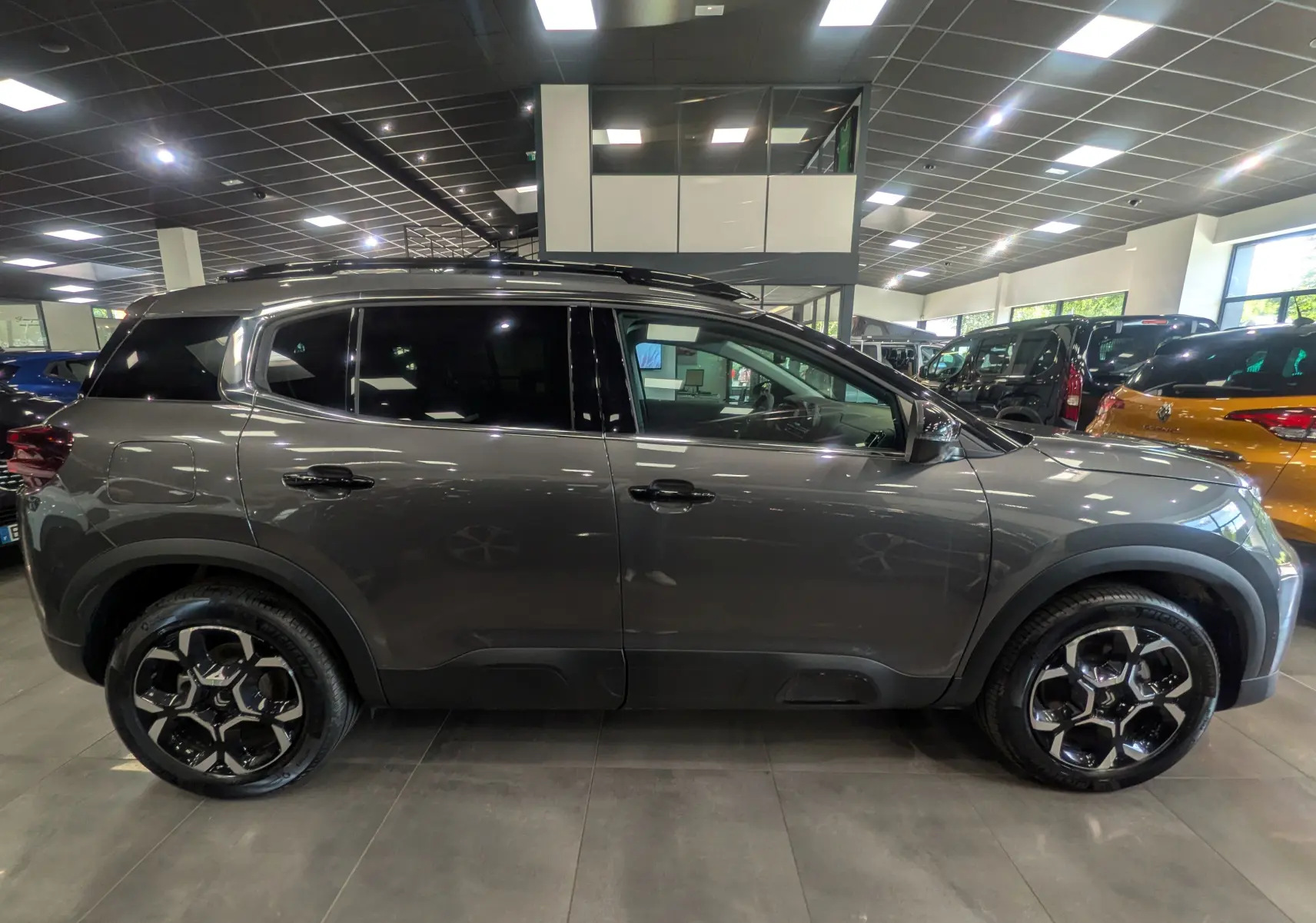 Vue de profil côté gauche d'un Citroën C5 Aircross hybride gris Platinium avec jantes noires et toit noir en concession.