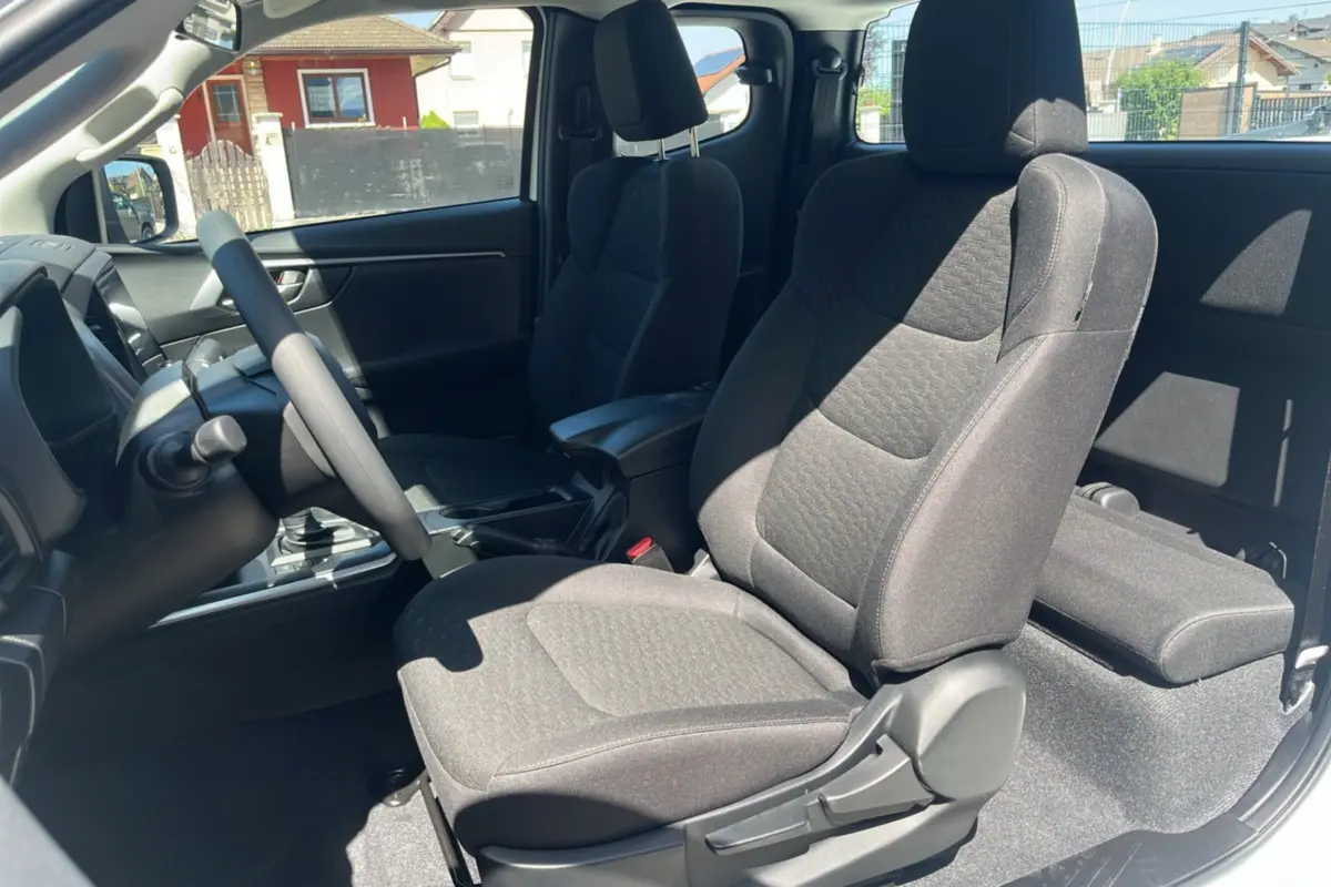 Vue intérieure côté conducteur du pick-up Isuzu D-MAX 2026, sièges tissu gris avec accoudoir central avant.