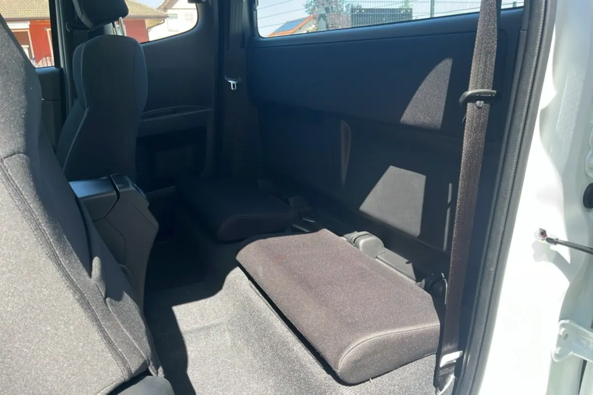 Vue intérieure arrière côté droit du pick-up Isuzu D-MAX 2026 blanc, banquette arrière rabattue en tissu noir.