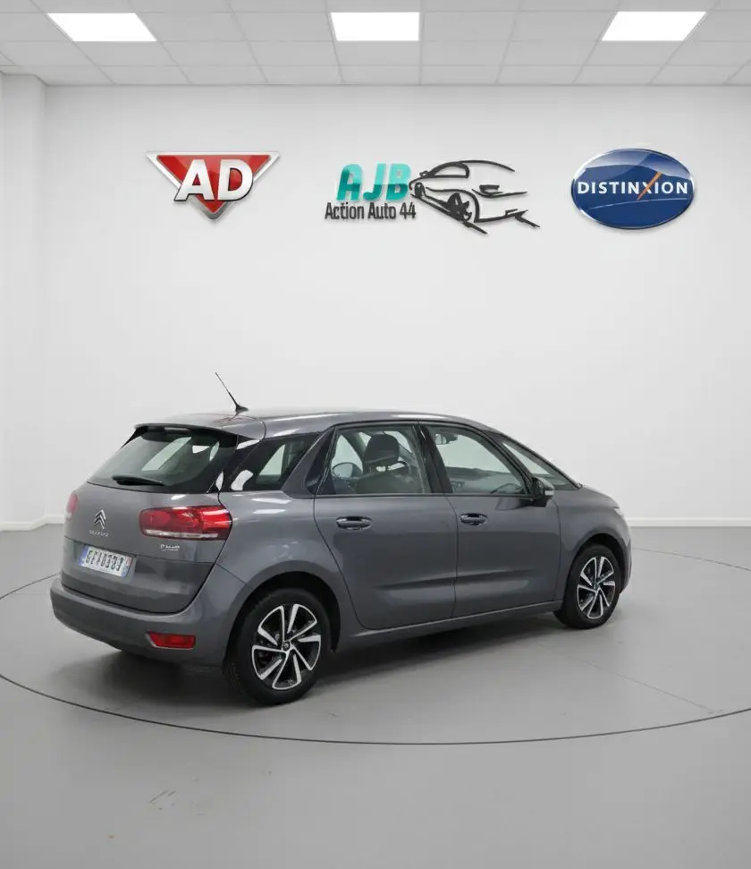 Vue 3/4 arrière gauche d'une Citroën C4 Picasso marron 2017 avec porte avant gauche ouverte sur parking humide.