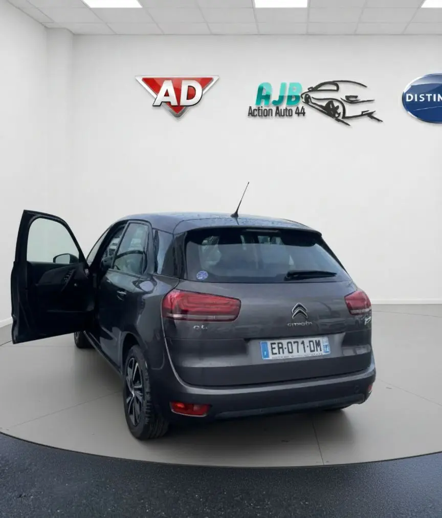 Vue de profil côté gauche d'une Citroën C4 Picasso marron avec porte avant ouverte et jantes alu sur sol humide.