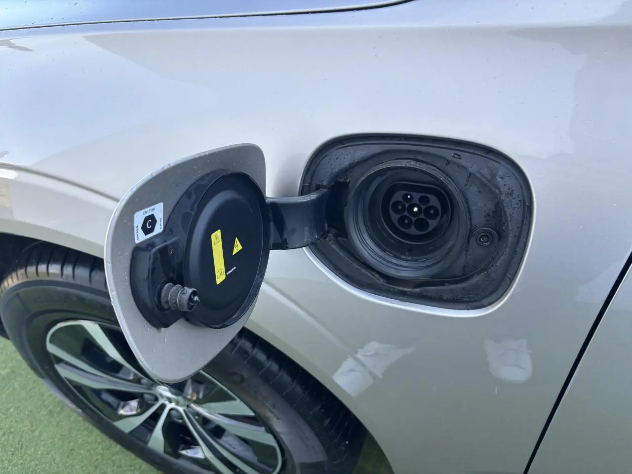 Prise de recharge ouverte côté gauche d'un Volvo XC60 argent crépuscule métallisé, jante alliage visible.