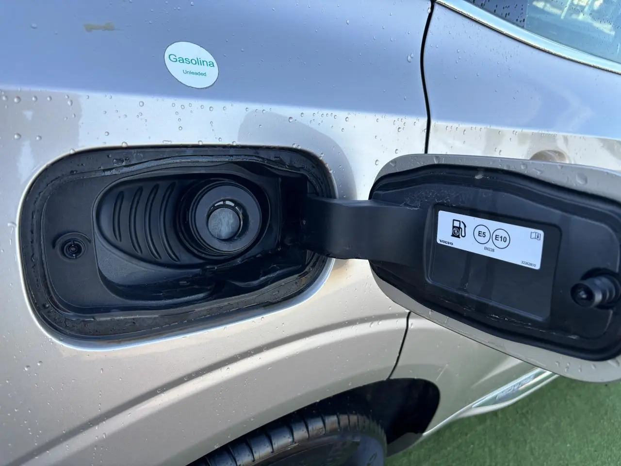 Détail de la trappe à carburant ouverte côté gauche d’un Volvo XC60 argent crépuscule métal avec gouttes d’eau.