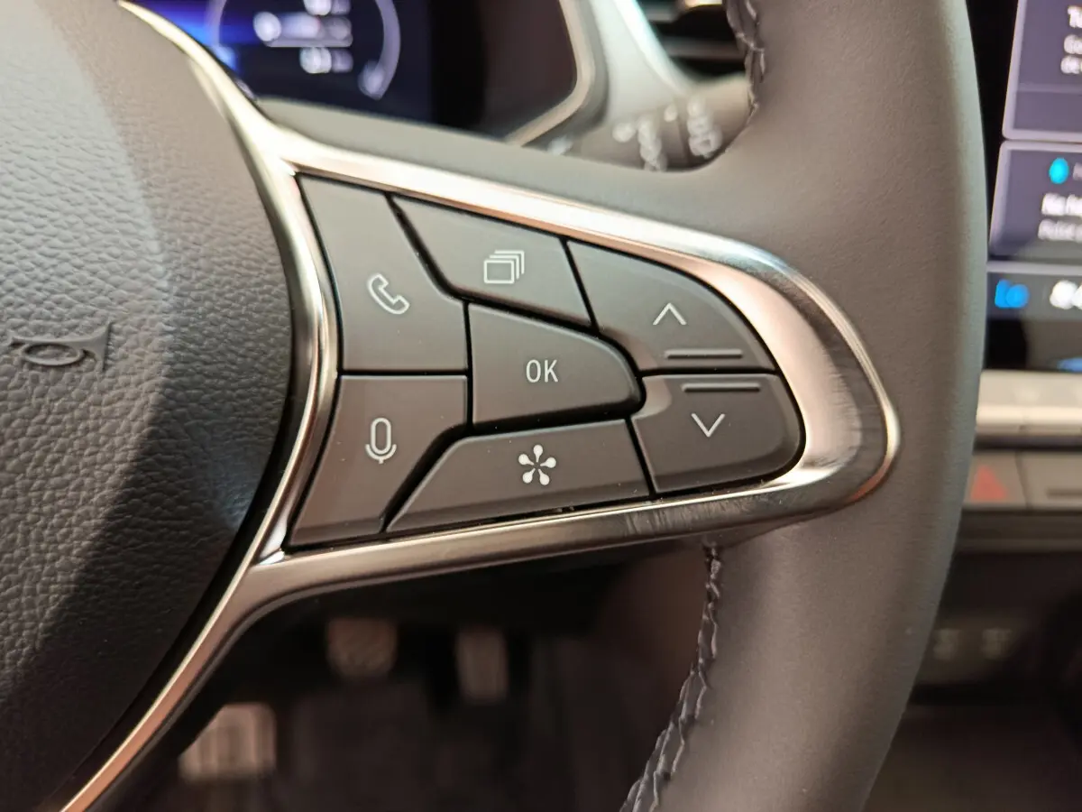 Gros plan sur les commandes multifonctions à droite du volant noir du Renault Captur gris foncé 2025 avec écran tactile visible.