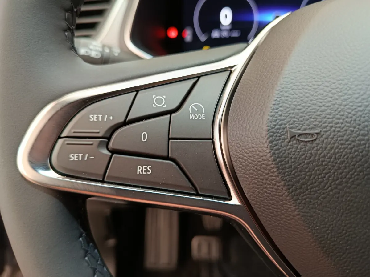 Gros plan sur les commandes du volant côté gauche du Renault Captur gris foncé, avec affichage numérique en arrière-plan.