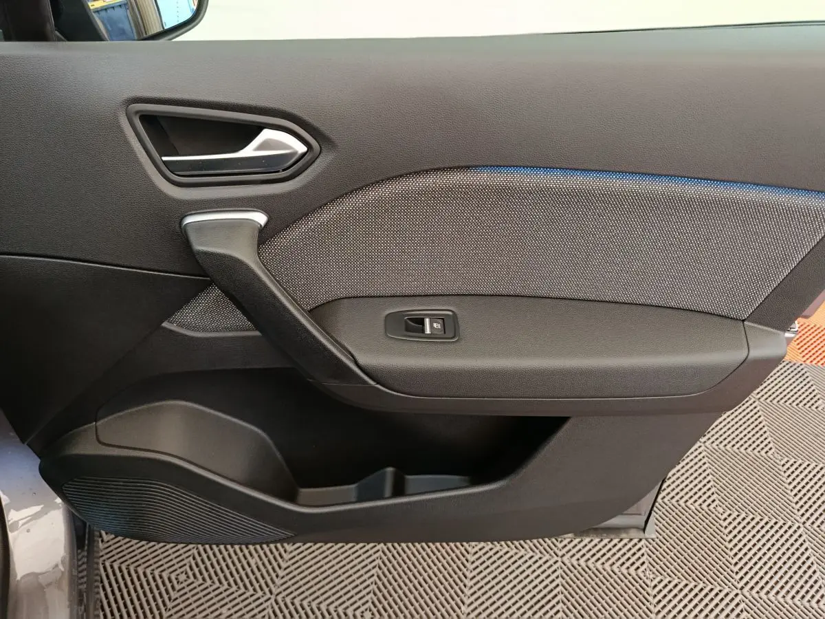 Gros plan sur la porte côté gauche du Renault Captur gris foncé, montrant la poignée et le bouton de lève-vitre.