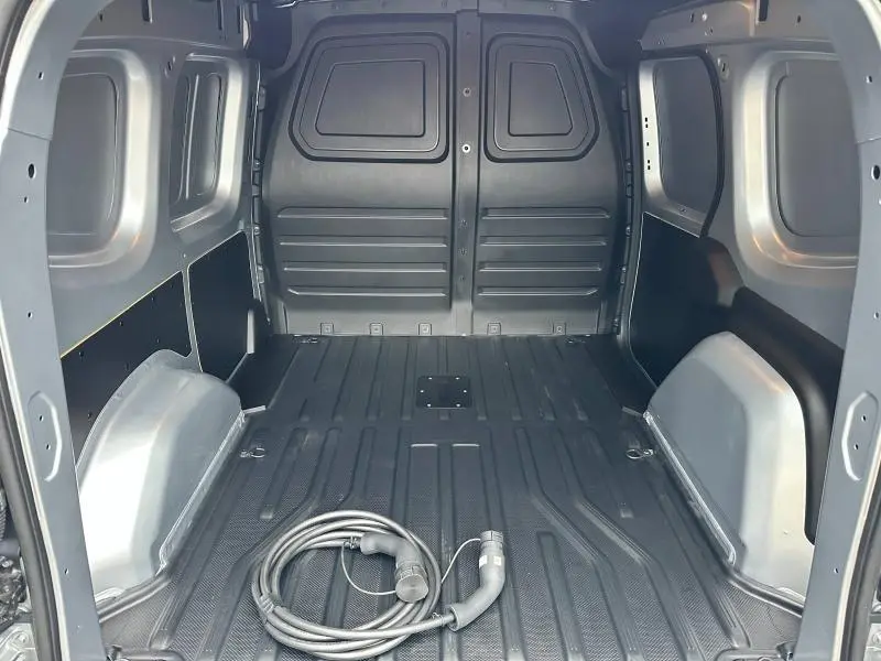 Vue intérieure arrière du coffre gris du Nissan Townstar électrique 2024 avec câble de charge posé au sol.