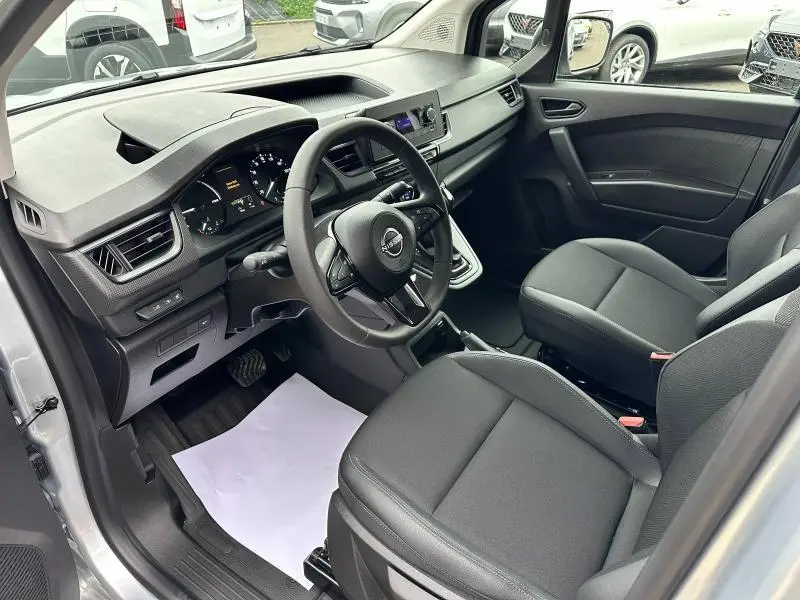 Intérieur avant droit du Nissan Townstar gris 2024, tableau de bord moderne et sièges en tissu noir visibles.