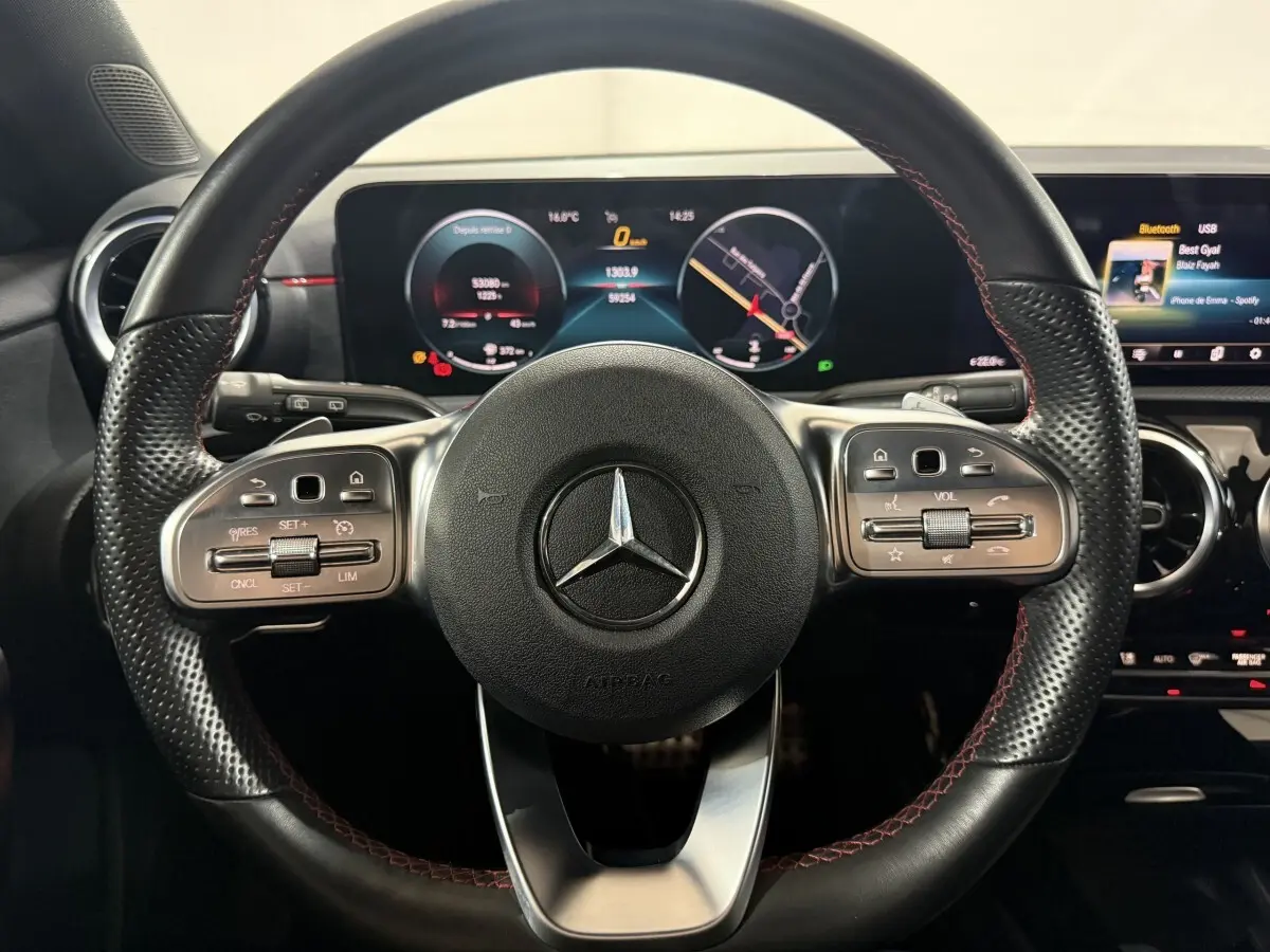 Vue rapprochée du volant cuir noir avec surpiqûres rouges et tableau de bord numérique d’une Mercedes Classe A AMG Line 2021.