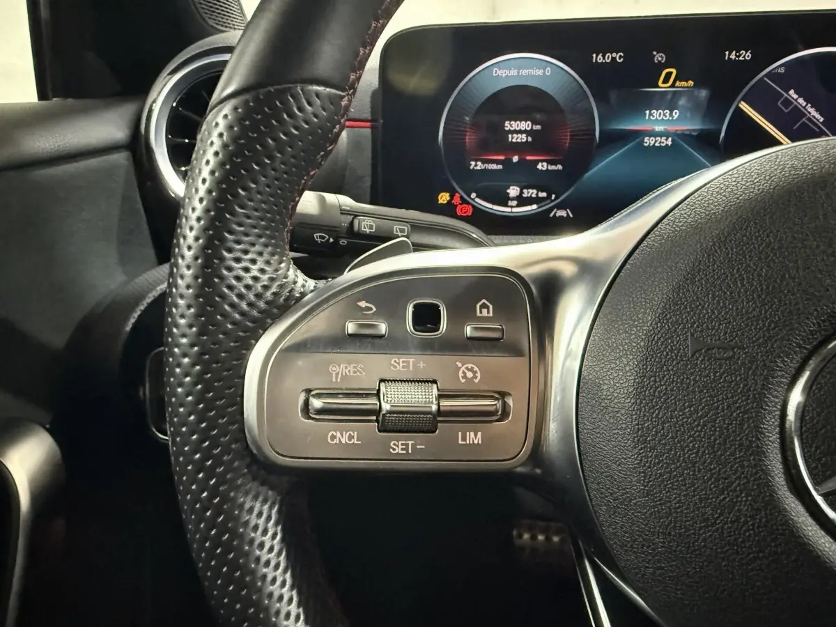 Gros plan sur le volant cuir perforé côté gauche d’une Mercedes Classe A 200 AMG Line 2021 avec tableau de bord numérique allumé.
