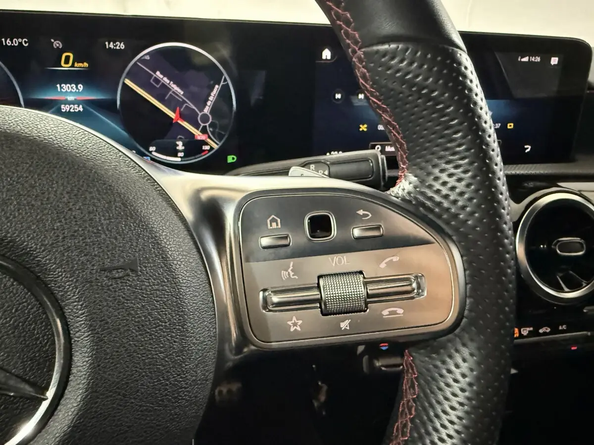 Gros plan sur le volant cuir perforé avec surpiqûres rouges et tableau de bord numérique de la Mercedes Classe A AMG Line gris foncé.