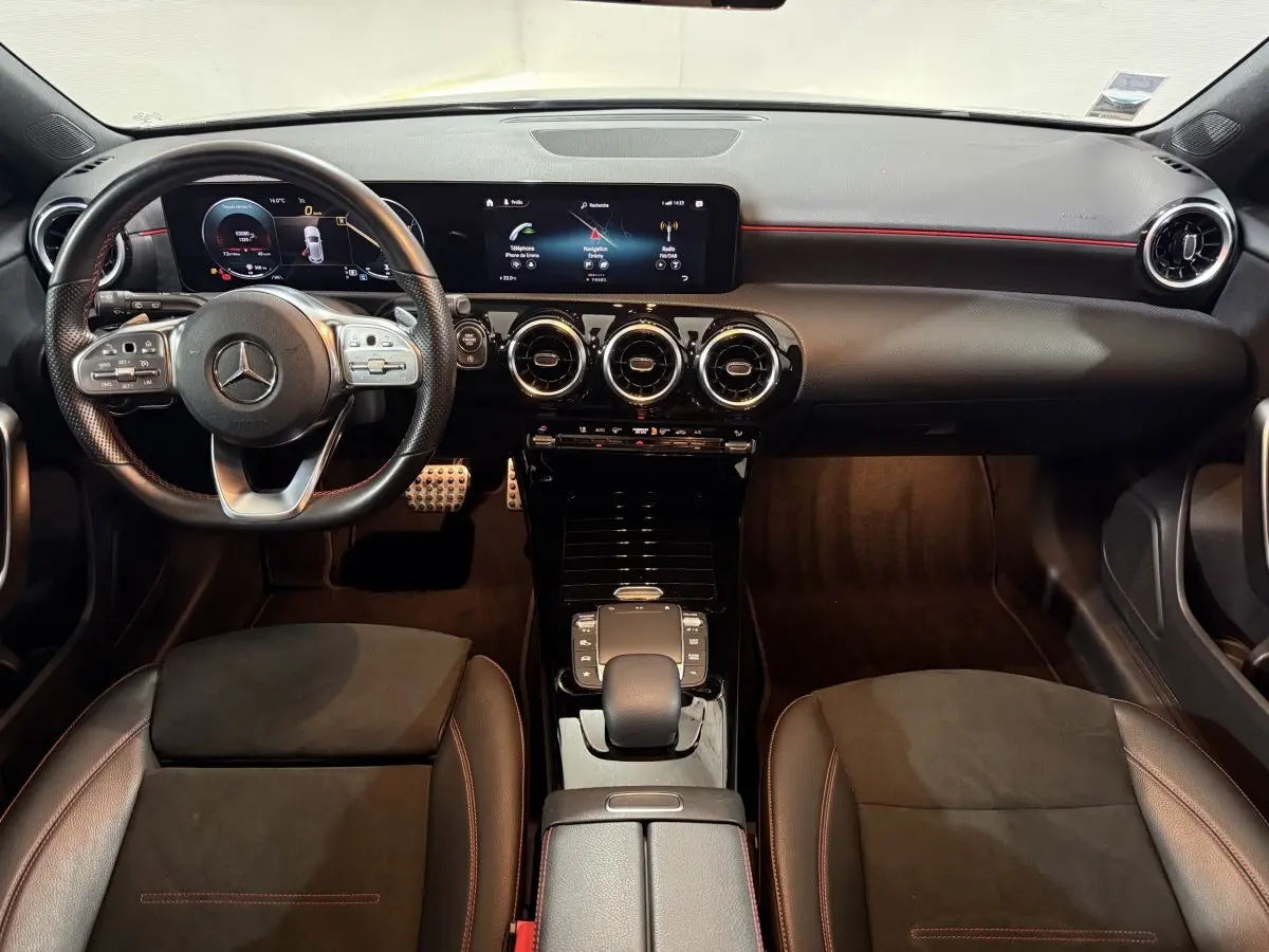 Vue intérieure avant de la Mercedes Classe A A 200 AMG Line 2021, tableau de bord noir avec écrans numériques et volant cuir.
