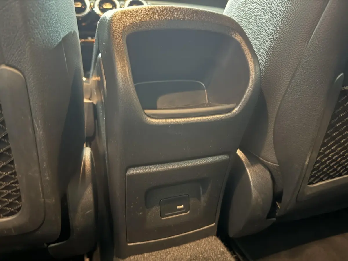 Vue rapprochée de la console centrale arrière noire avec port USB entre les sièges arrière d'une Mercedes Classe A gris foncé.