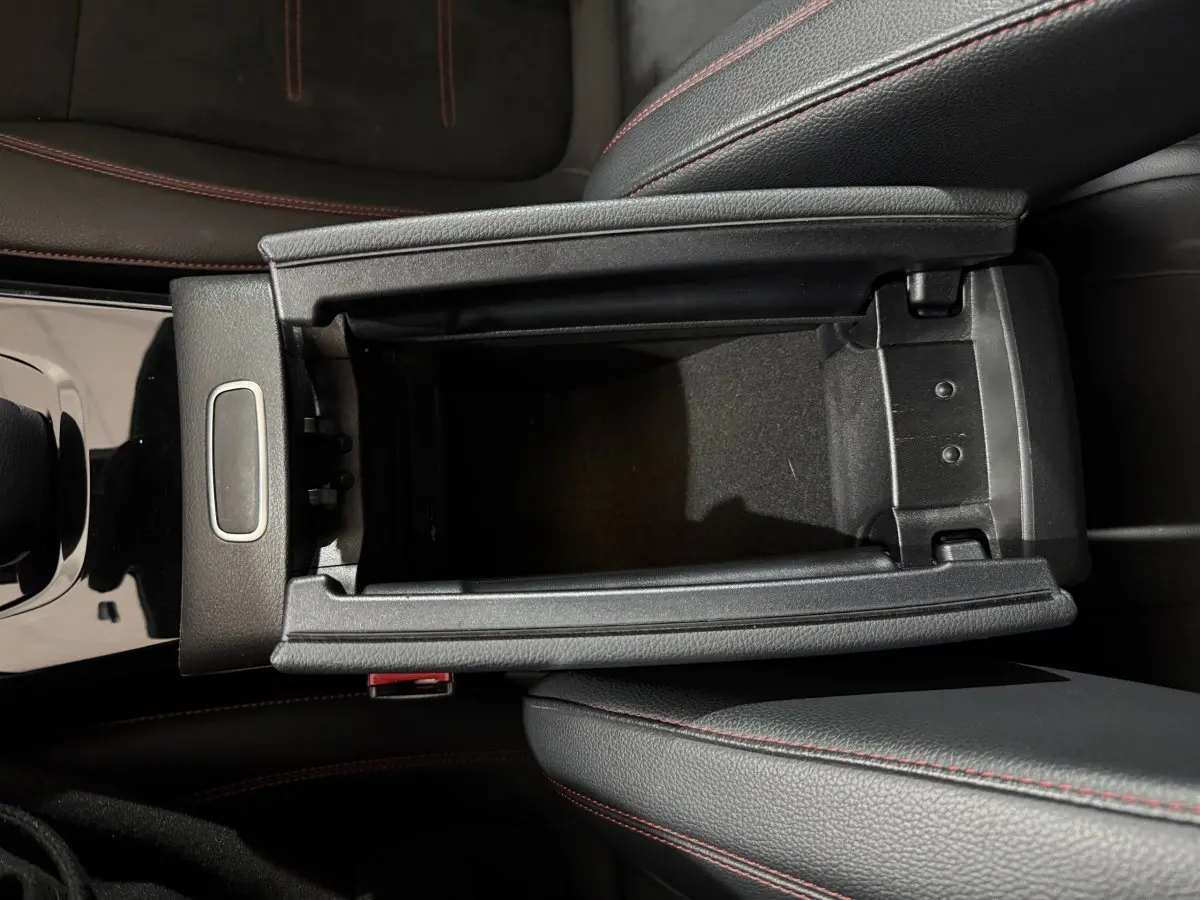Vue plongeante sur la console centrale noire avec rangement ouvert et surpiqûres rouges des sièges cuir d’une Mercedes Classe A AMG Line.