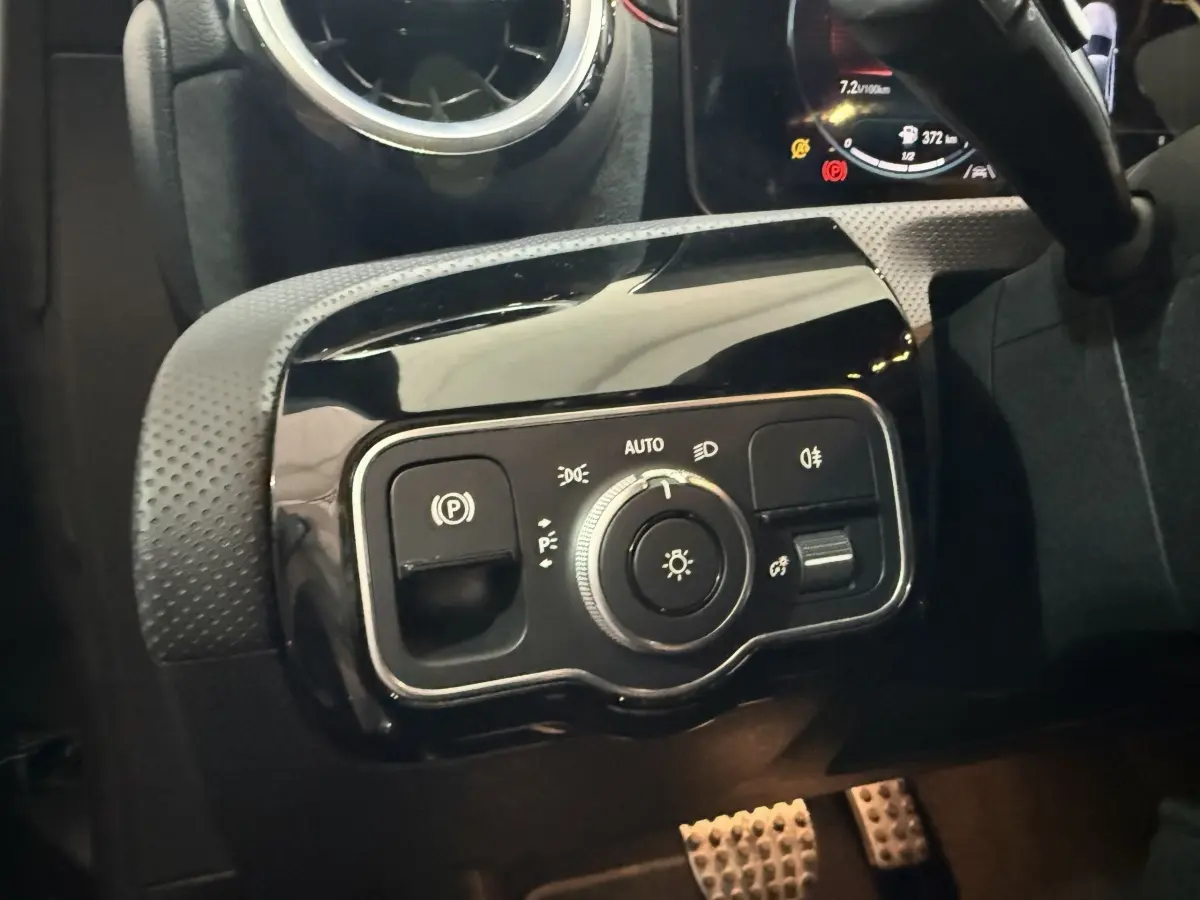 Gros plan sur le panneau de commande des phares et frein à main électrique, intérieur noir d'une Mercedes Classe A AMG Line 2021.