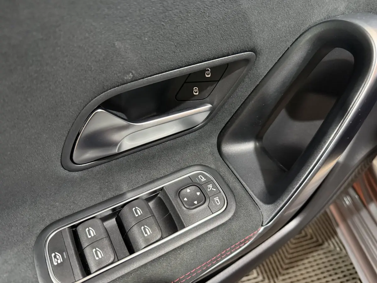 Poignée intérieure et commandes des vitres côté gauche en tissu noir avec surpiqûres rouges dans une Mercedes Classe A AMG Line gris foncé.