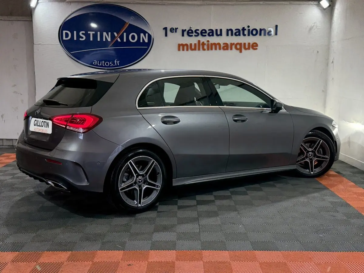 Vue latérale droite d'une Mercedes Classe A 200 AMG Line gris foncé en intérieur, avec jantes alliage et feux arrière LED allumés.