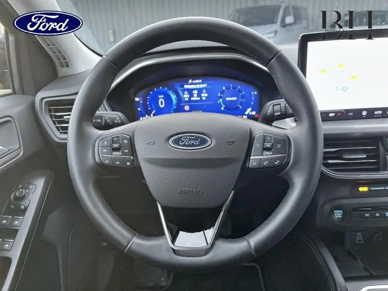Vue centrée sur le volant cuir multifonction de la Ford Focus SW 2024 avec tableau de bord numérique bleu et écran tactile.