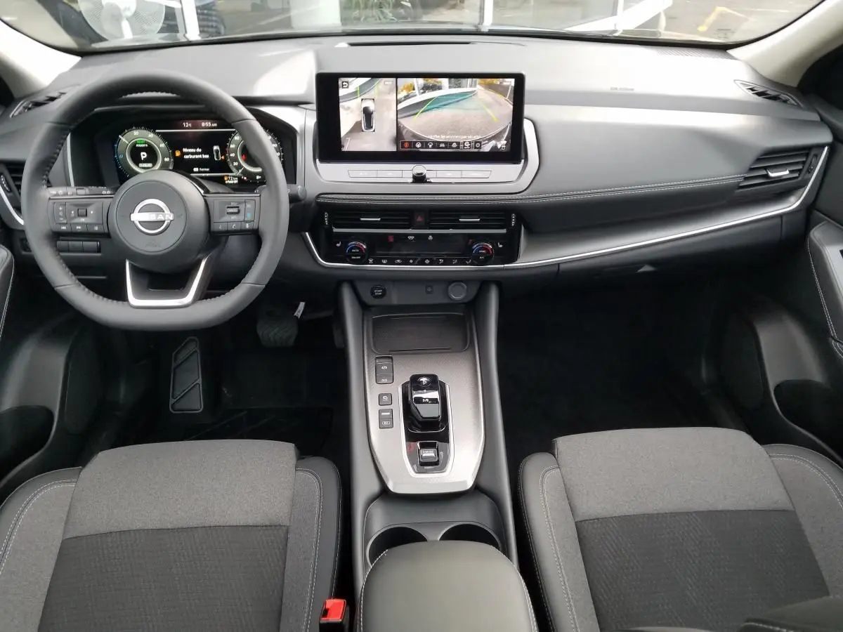 Vue intérieure avant du Nissan Qashqai 1.5 E-POWER 2025, tableau de bord noir avec écran central et volant multifonction.