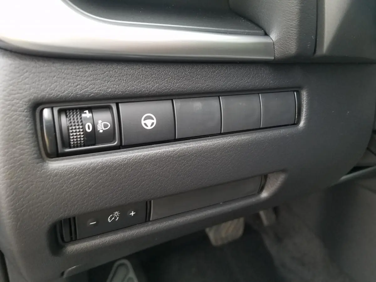 Gros plan sur les commandes de réglage des phares et assistance au volant du Nissan Qashqai noir, côté conducteur.