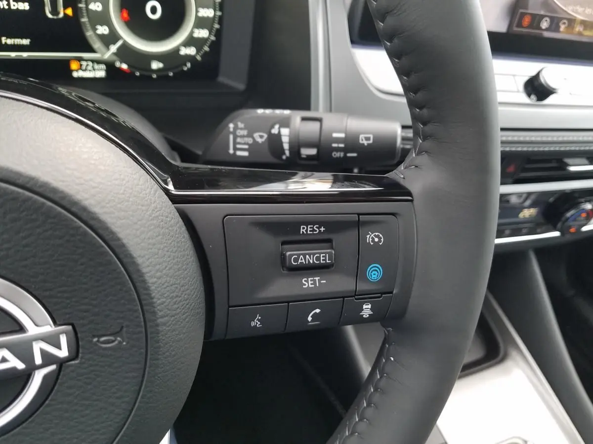 Gros plan sur le volant noir du Nissan Qashqai 2025, avec commandes de régulateur de vitesse et tableau de bord numérique en arrière-plan.