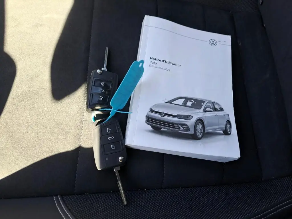 Notice d'utilisation Volkswagen Polo gris 3/4 avant sur siège noir avec deux clés de voiture posées à côté.