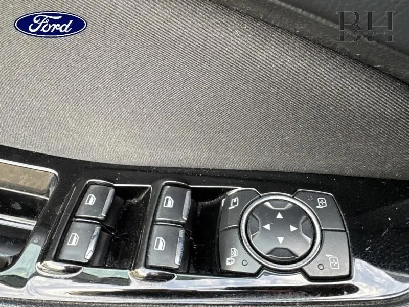 Gros plan sur les commandes de lève-vitres et réglage des rétroviseurs côté conducteur d'un Ford S-MAX noir.