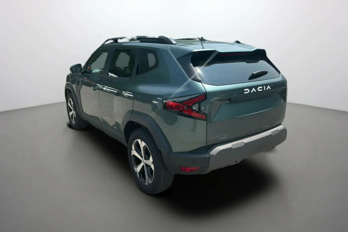 Vue 3/4 arrière droite du Dacia Duster 2025 vert cèdre avec jantes alu 18 pouces et barres de toit noires.