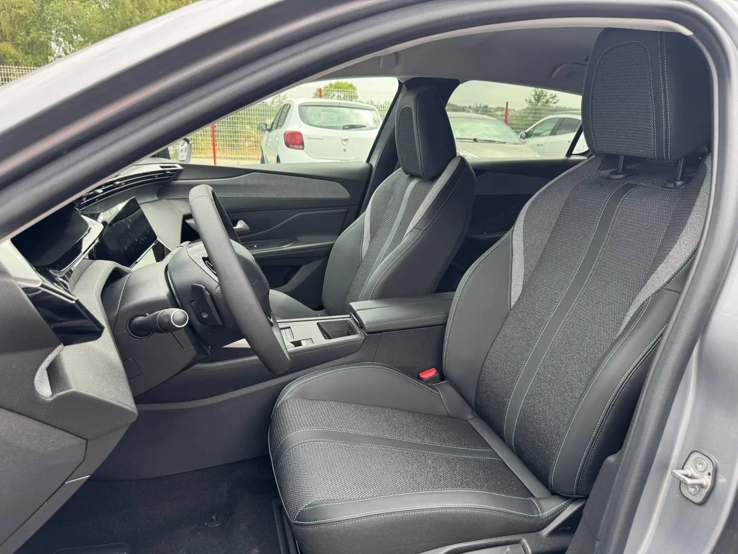 Vue intérieure côté conducteur de la Peugeot 308 1.2 Hybrid 145ch Allure gris Artense, sièges tissu et cuir noir avec surpiqûres.