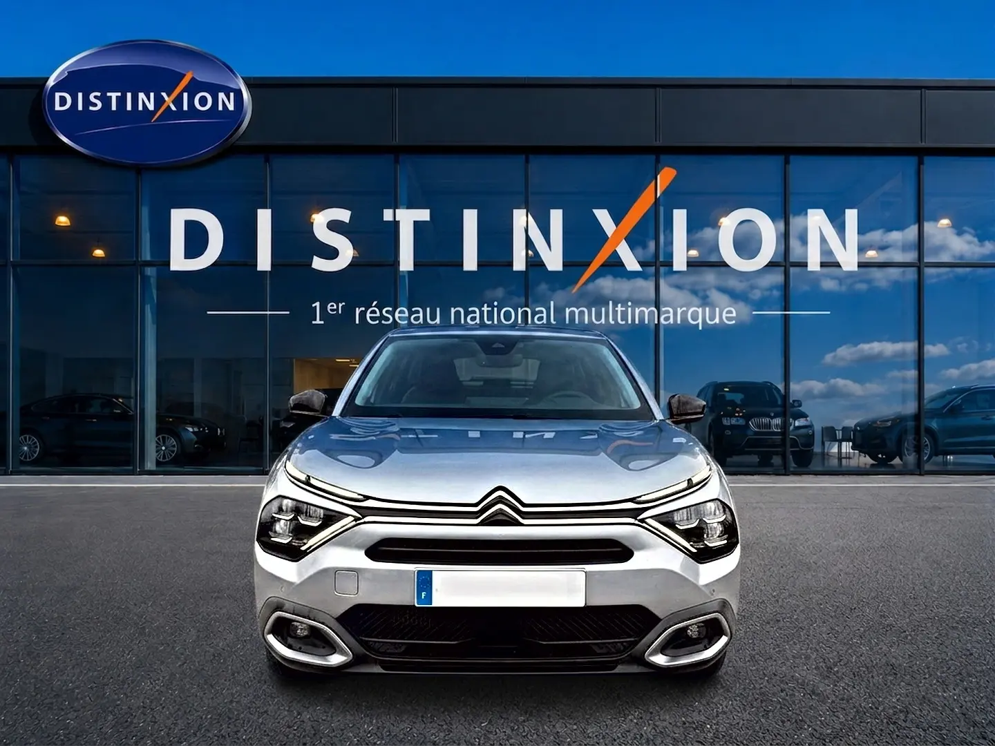 Citroën C4 gris vue de face, avec phares LED distinctifs, garée devant une vitrine Distinxion.