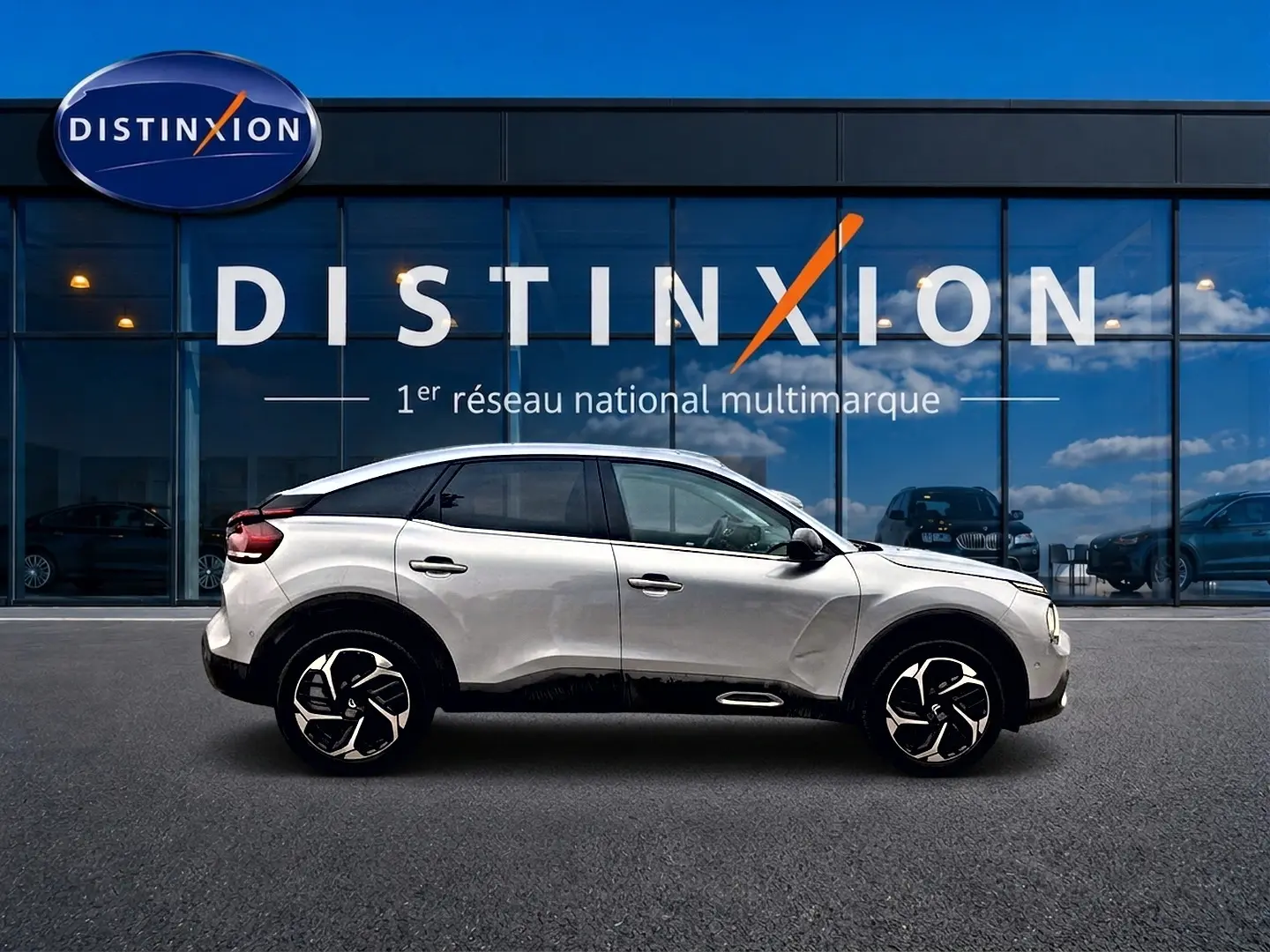 Profil droit d'une Citroën C4 gris clair 2024 avec jantes alu et vitres arrière surteintées devant une vitrine Distinxion.