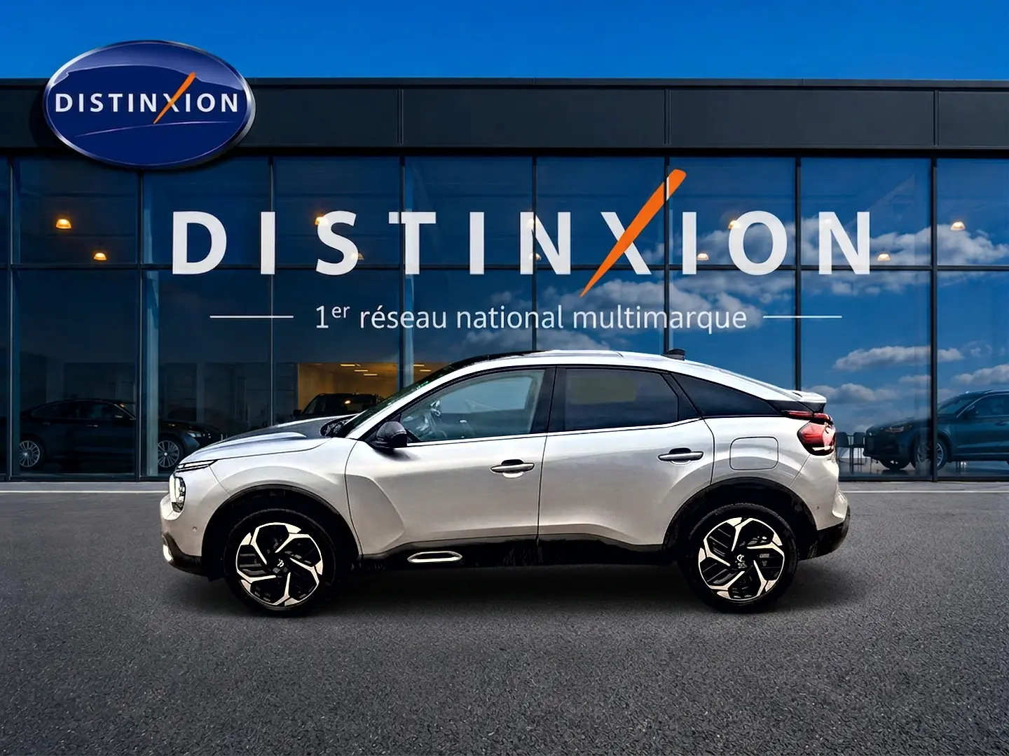 Profil droit d'une Citroën C4 gris clair 2024 avec jantes noires et toit noir devant une vitrine Distinxion.