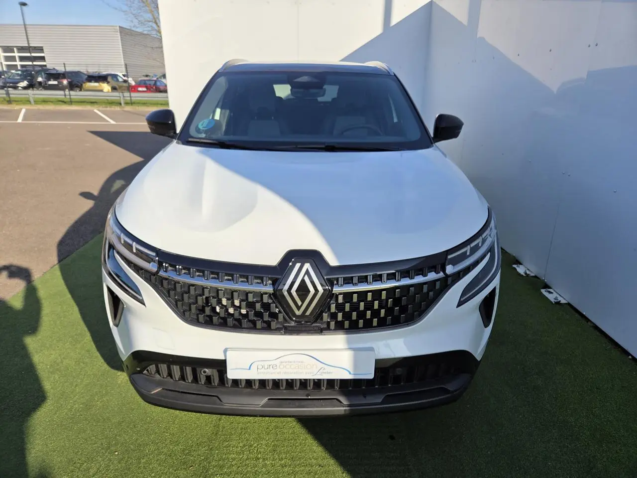 Vue avant d'un Renault Austral blanc nacré avec toit noir, mettant en valeur sa calandre noire et ses phares LED distinctifs.