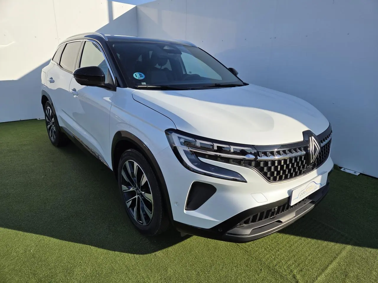 Renault Austral blanc nacré avec toit noir, vue 3/4 avant droit, jantes alliage noires et calandre distinctive.