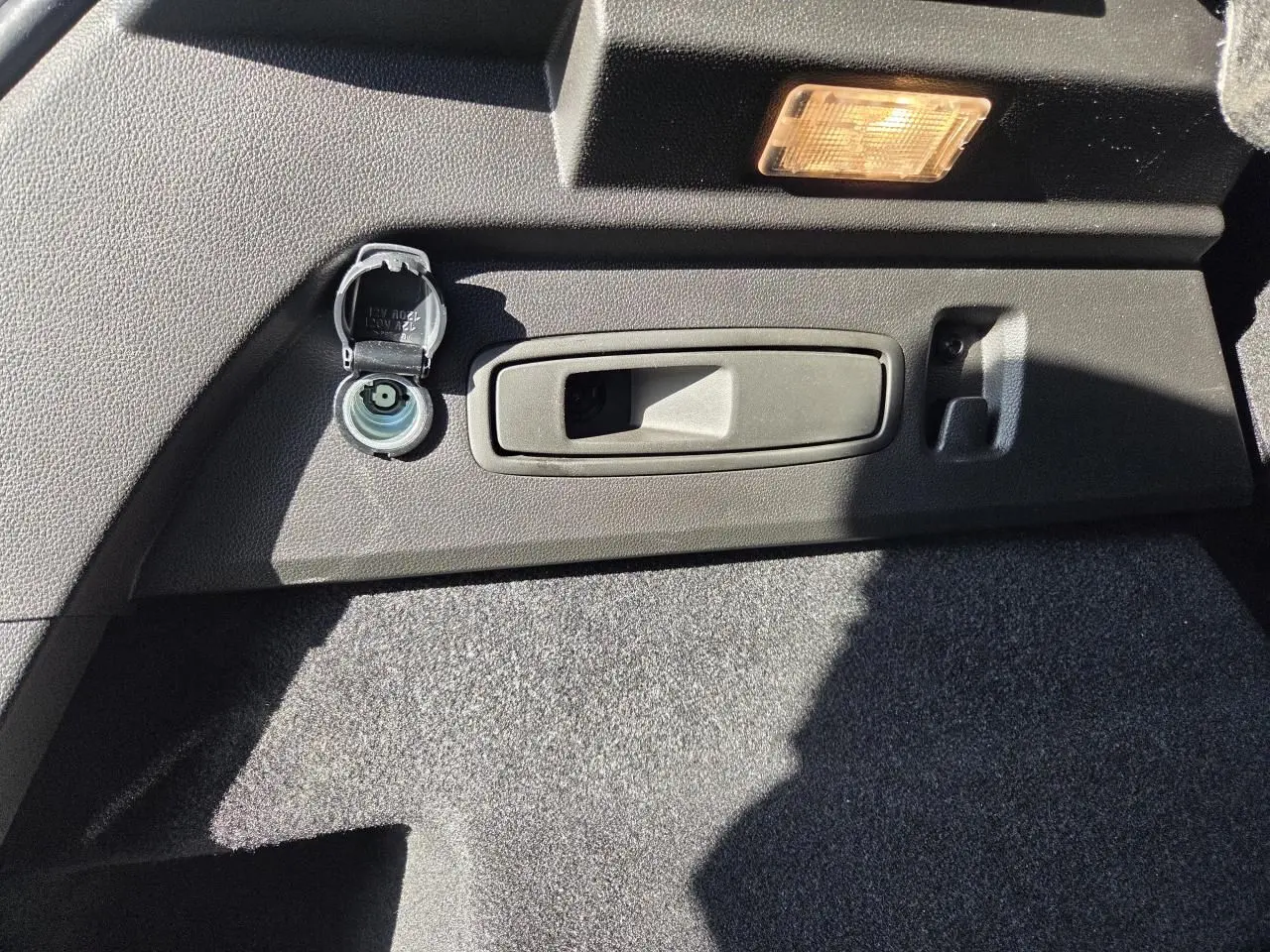 Détail de la prise 12V et poignée de coffre dans le coffre du Renault Austral blanc nacré 2025.