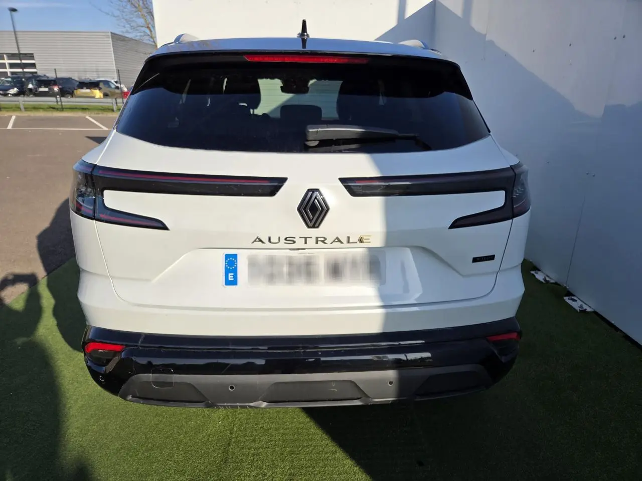 Vue arrière d'un Renault Austral blanc nacré avec toit noir, feux arrière horizontaux et logo central visible.