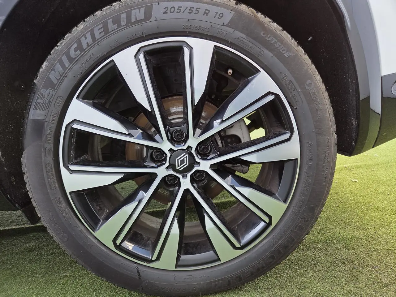 Gros plan sur la jante alliage 19 pouces diamantée noire du Renault Austral blanc nacré, avec pneu Michelin visible.