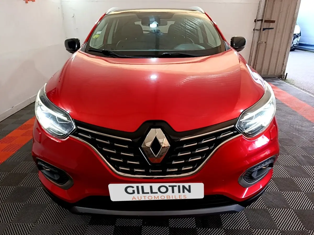 Vue avant d’un Renault Kadjar rouge avec calandre chromée et phares allumés dans un garage.