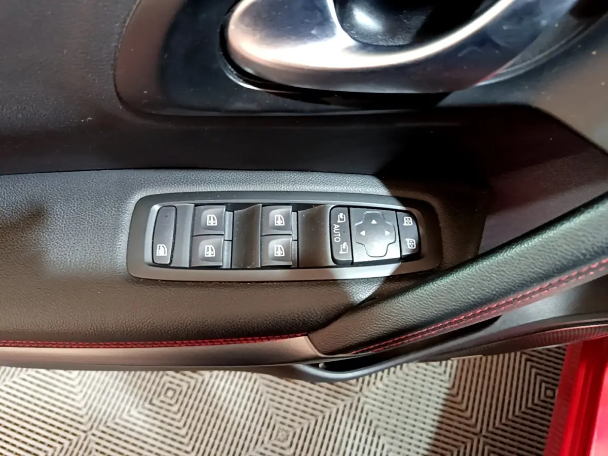 Gros plan sur les commandes de lève-vitres et rétroviseurs côté conducteur du Renault Kadjar rouge, intérieur noir avec surpiqûres rouges.