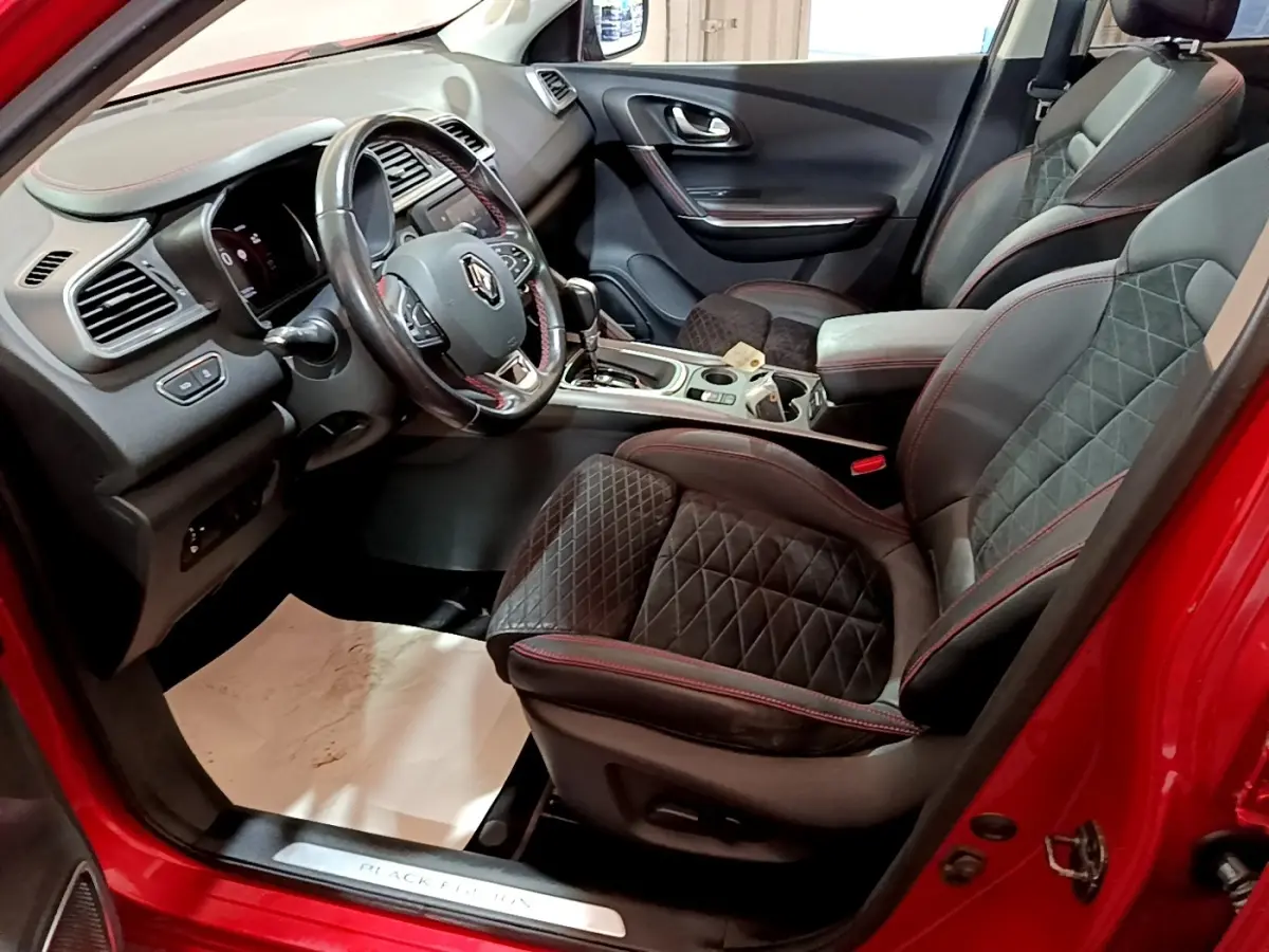 Vue intérieure côté conducteur du Renault Kadjar SL Black Edition rouge, mettant en valeur le volant cuir et les sièges noirs avec surpiqûres rouges.