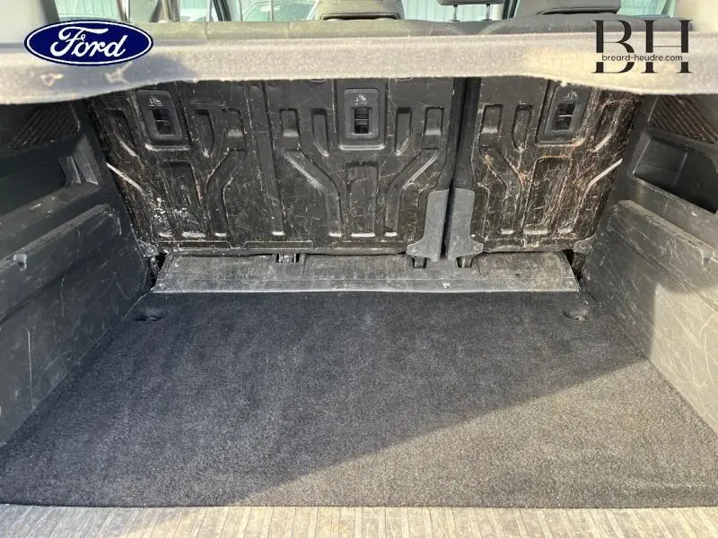 Coffre vu de l'intérieur avec tapis noir et parois arrière en plastique noir marqué, sans chargement visible.