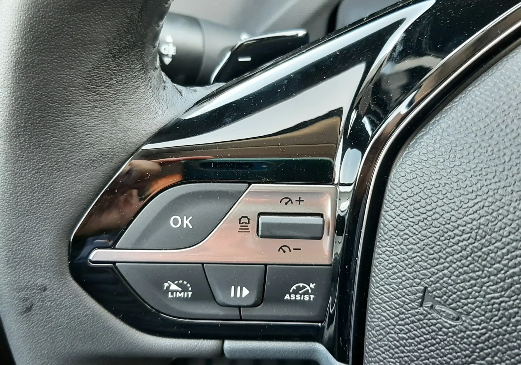 Gros plan sur les commandes gauche du volant noir d’une Peugeot 308 Bleu Obsession 2025 avec régulateur et assistant de conduite.