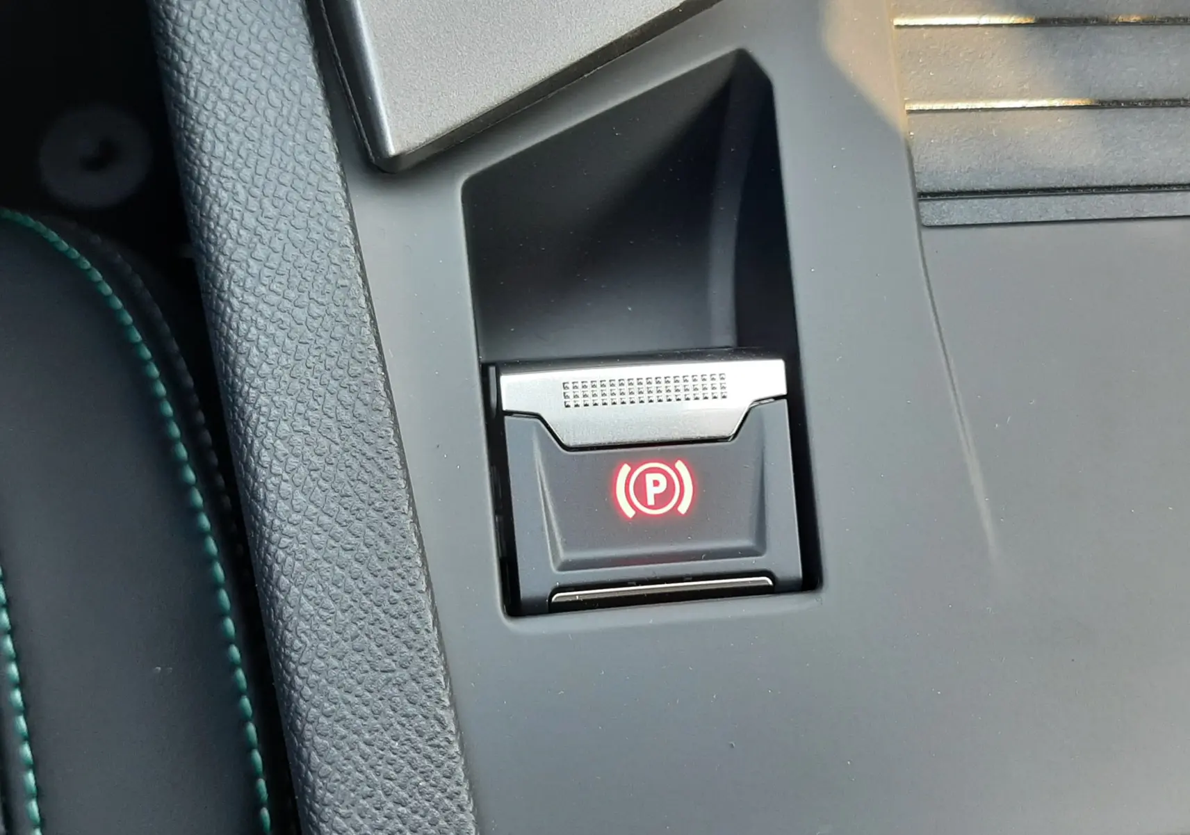 Gros plan sur le bouton de frein à main électrique rouge dans la console centrale d'une Peugeot 308 Bleu Obsession 2025.