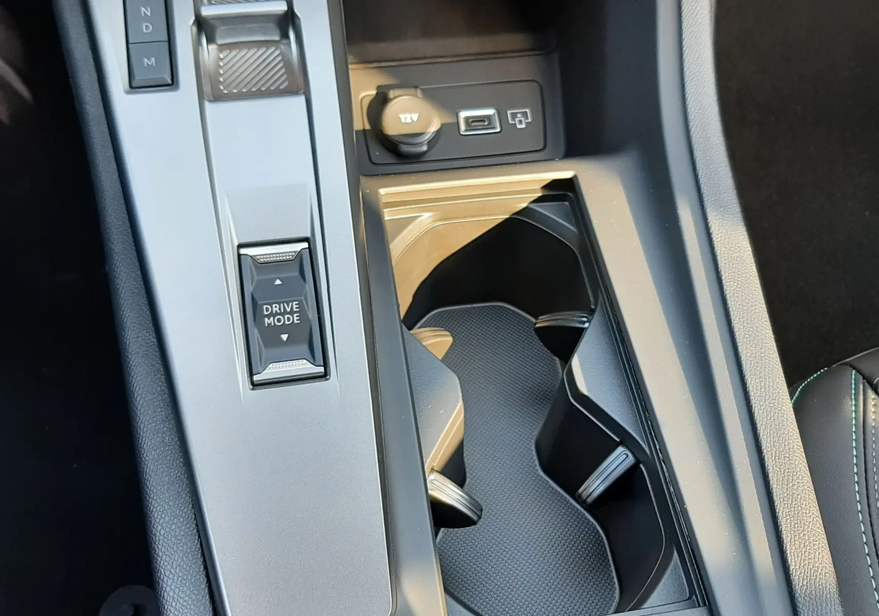 Vue rapprochée de la console centrale noire de la Peugeot 308 2025, avec sélecteur de mode de conduite et prises USB/12V.