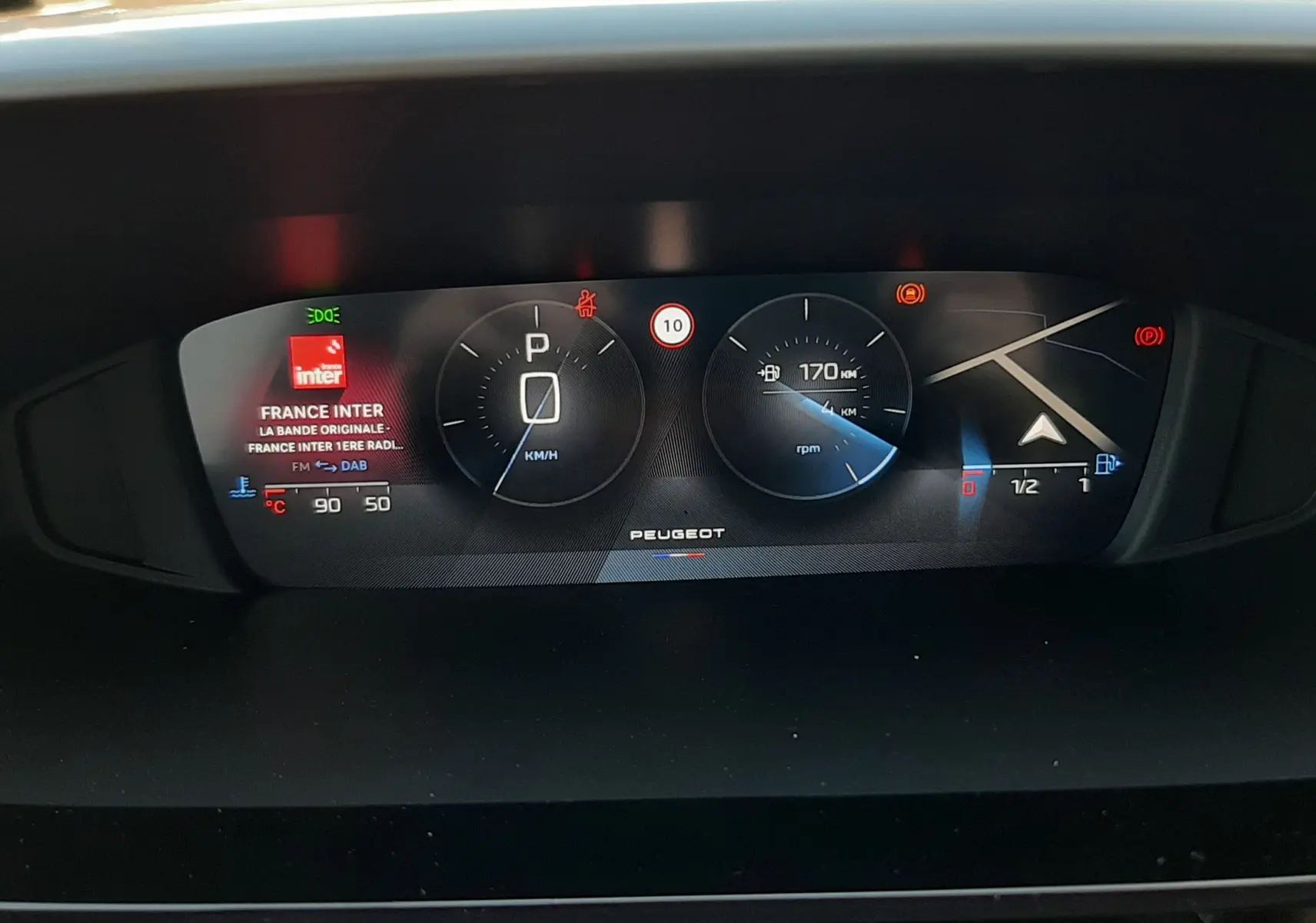 Tableau de bord numérique de Peugeot 308 Bleu Obsession, affichage central avec vitesse, navigation et radio visible.