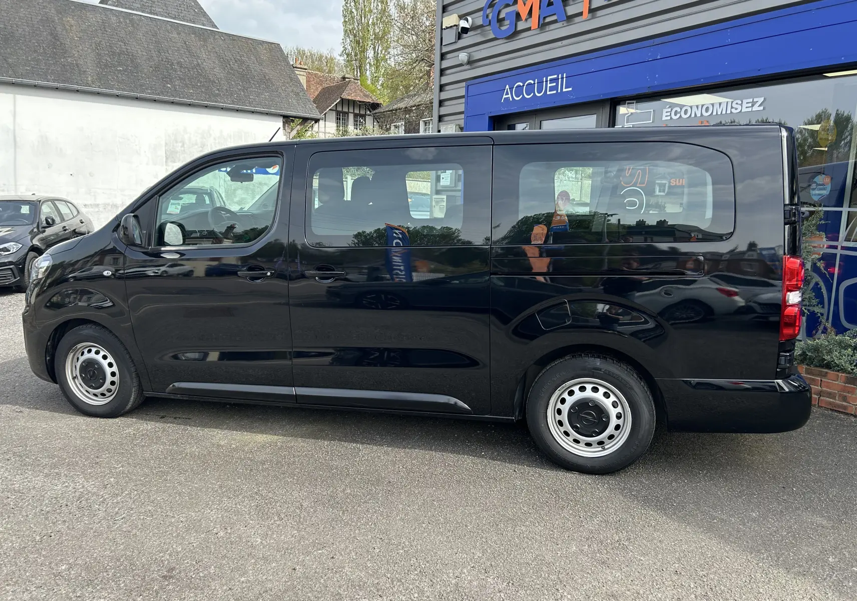 Opel Vivaro Combi noir vu de profil côté gauche, stationné devant un bâtiment avec vitrine bleue.