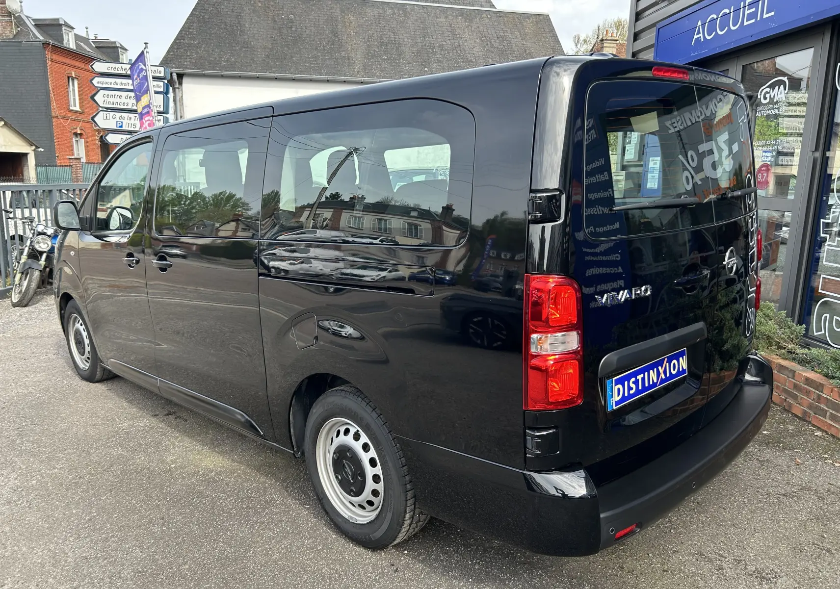 Vue 3/4 arrière droite d’un Opel Vivaro Combi noir garé devant un bâtiment avec vitrine et panneau d’accueil.