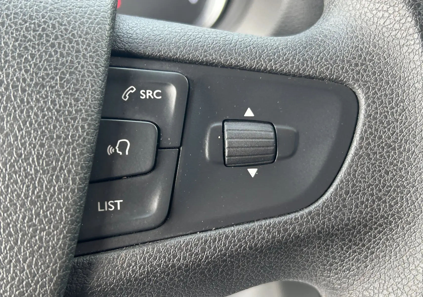 Gros plan sur les commandes noires au volant de l'Opel Vivaro Combi, boutons SRC, liste et molette de réglage.