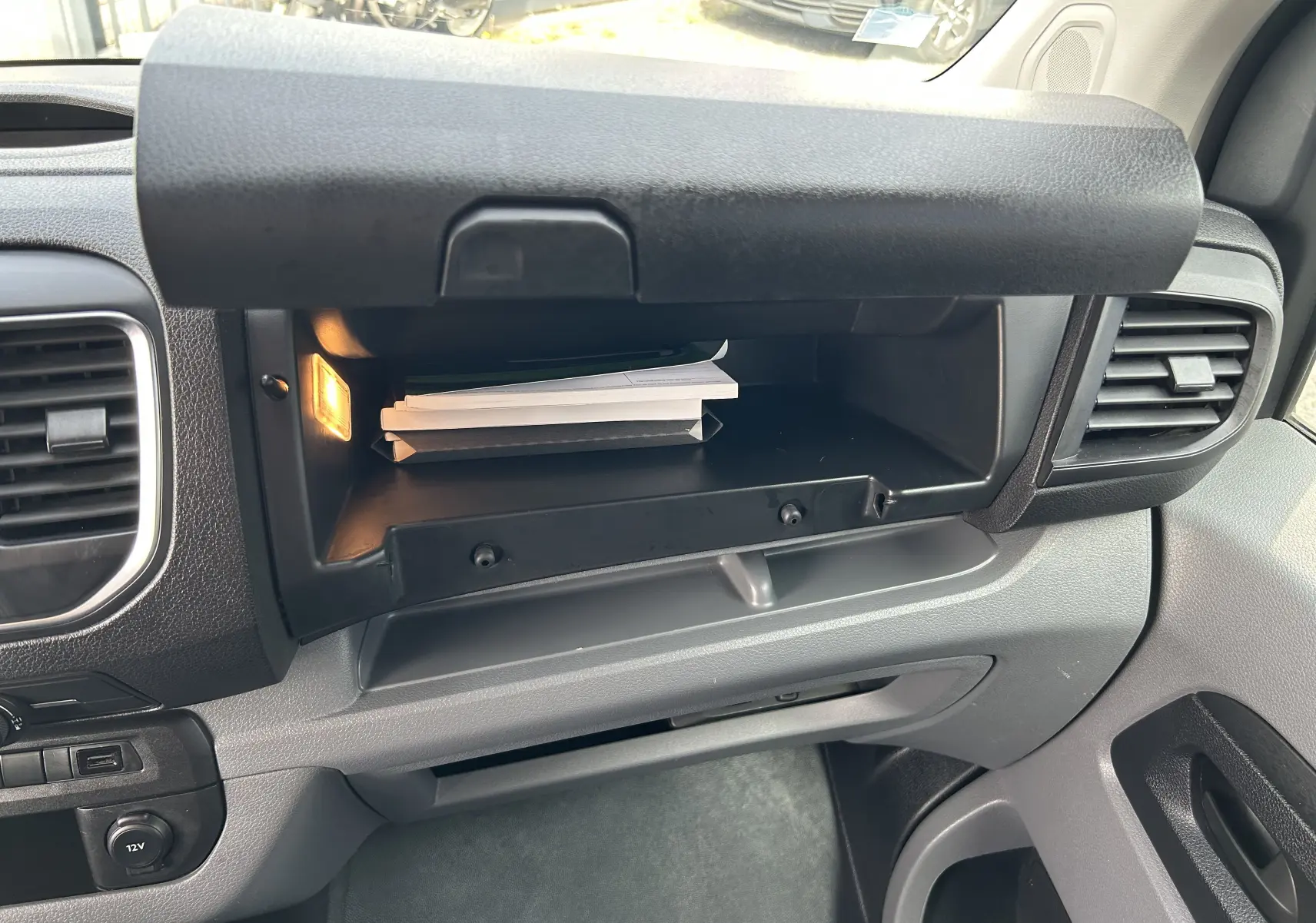 Vue intérieure du compartiment à gants ouvert de l'Opel Vivaro Combi noir, avec éclairage et documents visibles.